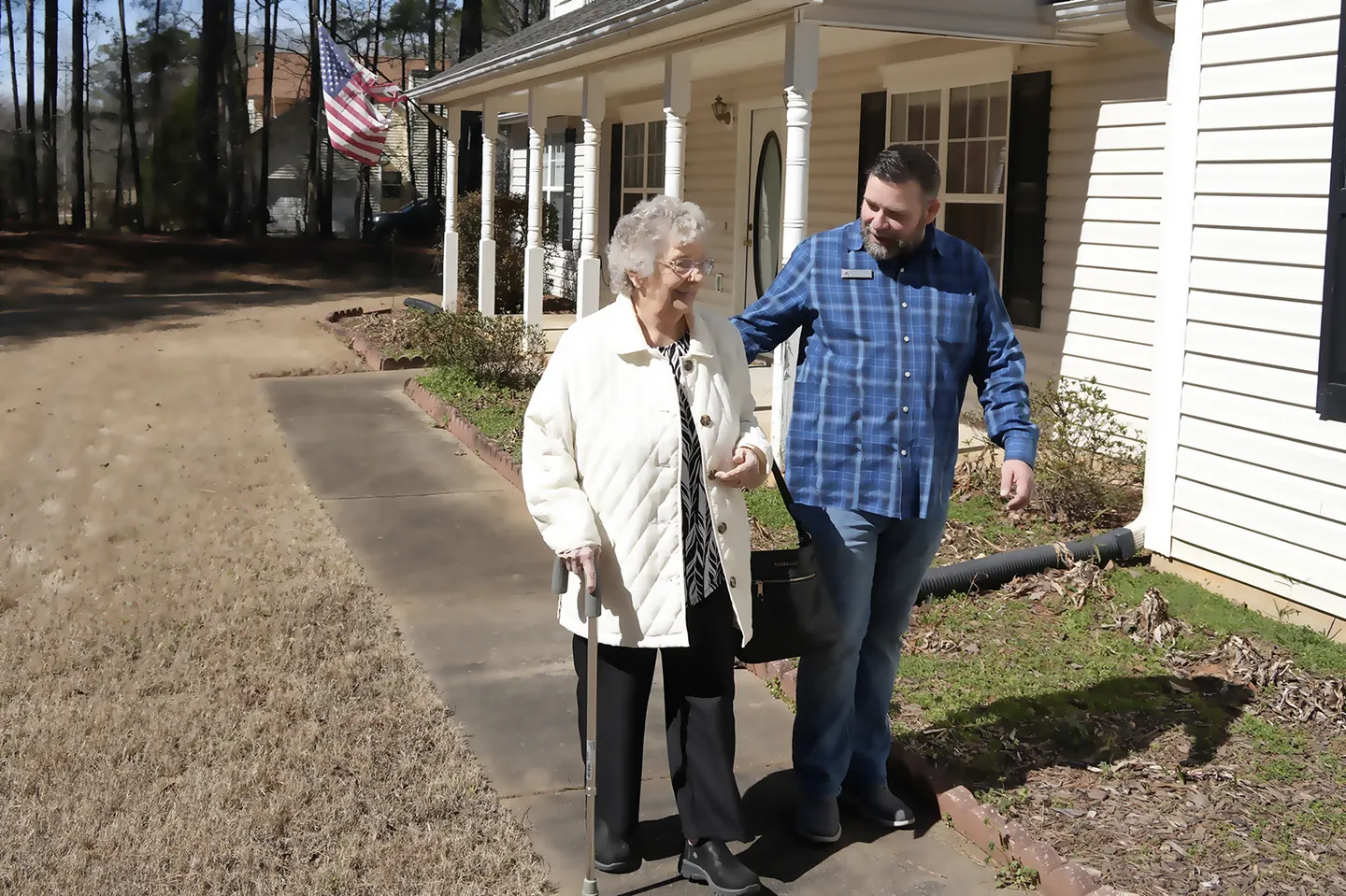 A volunteer walking a Neighbor along the sidewalk outside her home